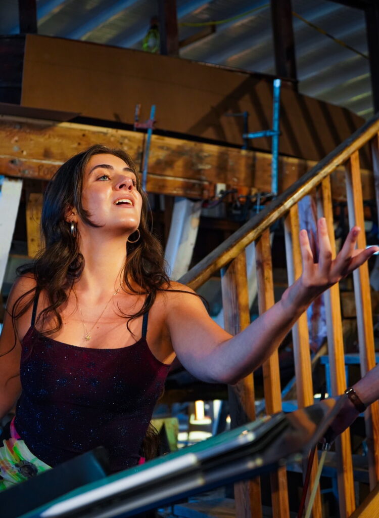 Young woman with long dark hair singing with a hand outstretched