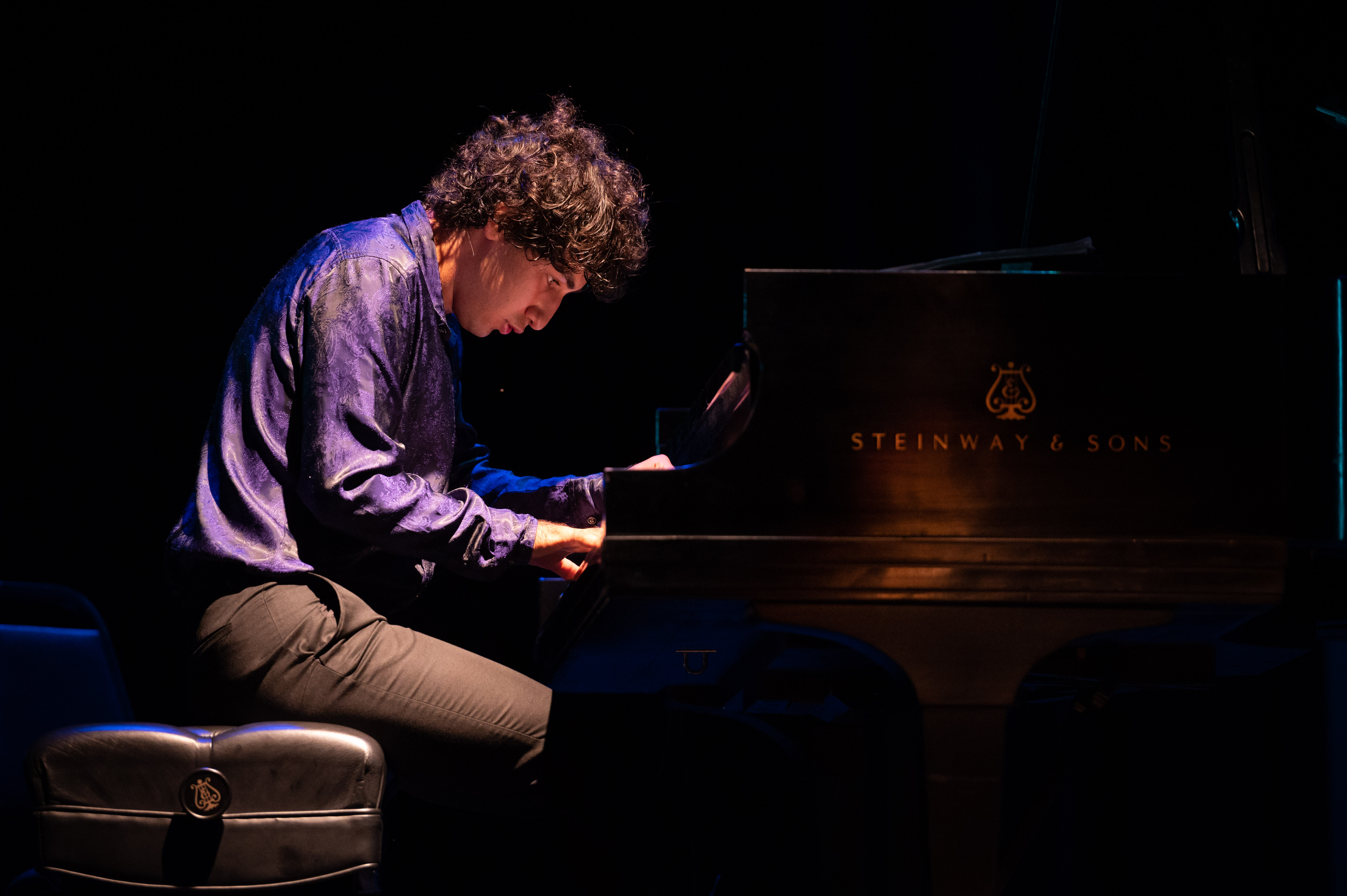 Young man bent over playing a piano on stage