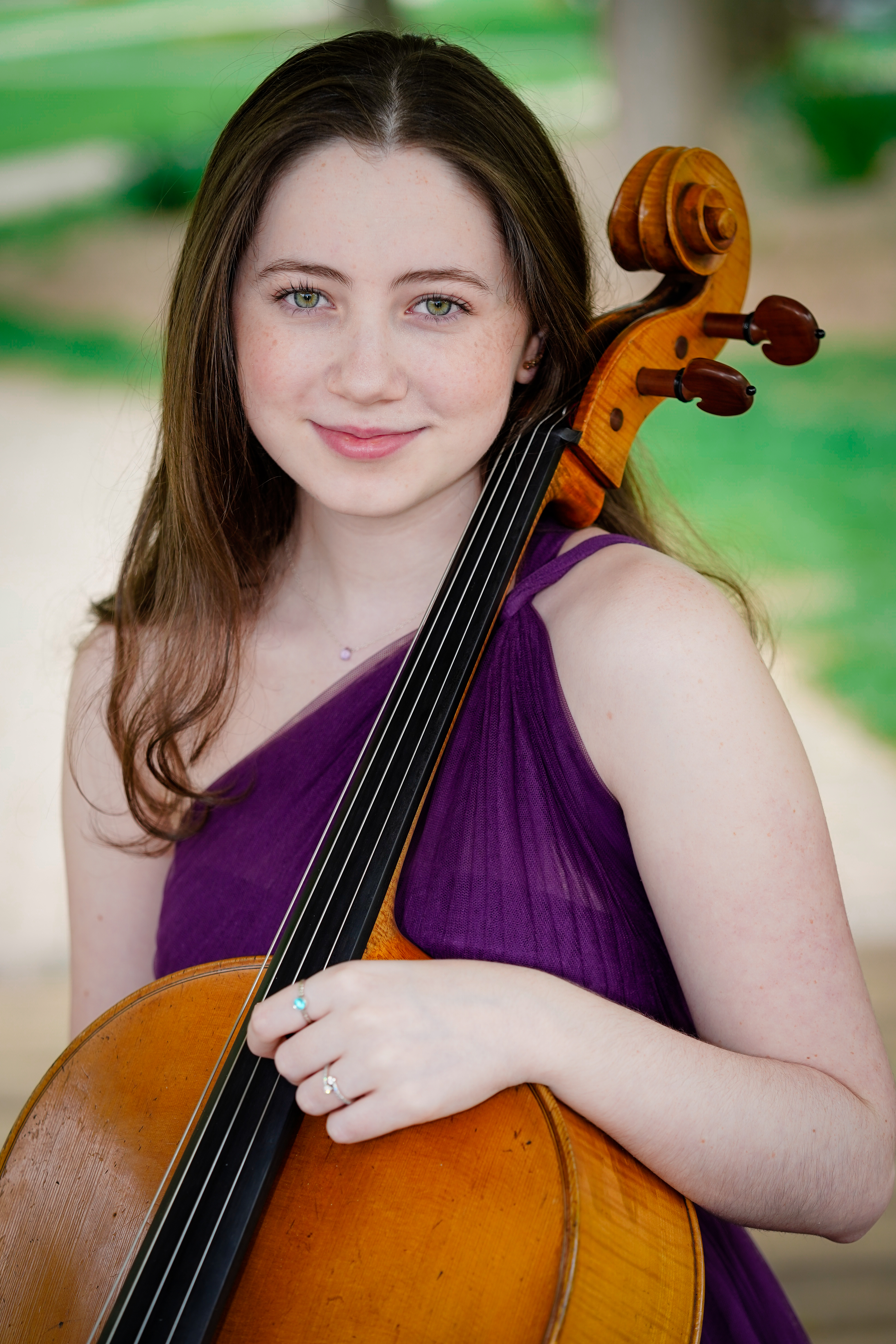 Young woman in purple one-shouldered top sitting with cello